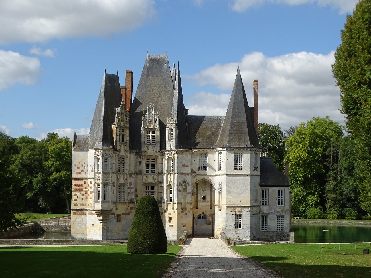 Le Chateau d'Ô: un château de plusieurs étages en pierre blanche avec un toit pentu en ardoises grises, entouré de l'eau